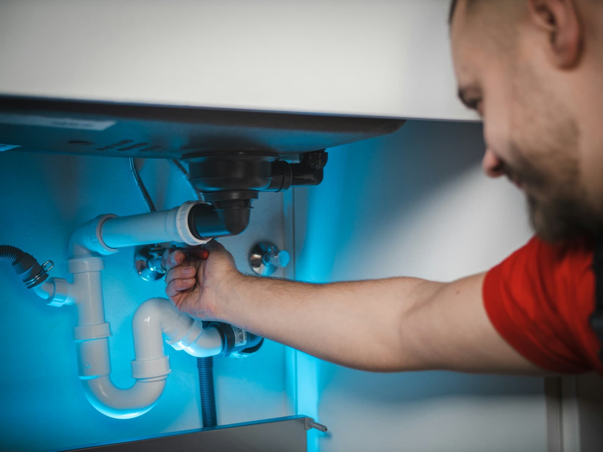 Stock photograph of a plumber repairing pipes beneath a sink